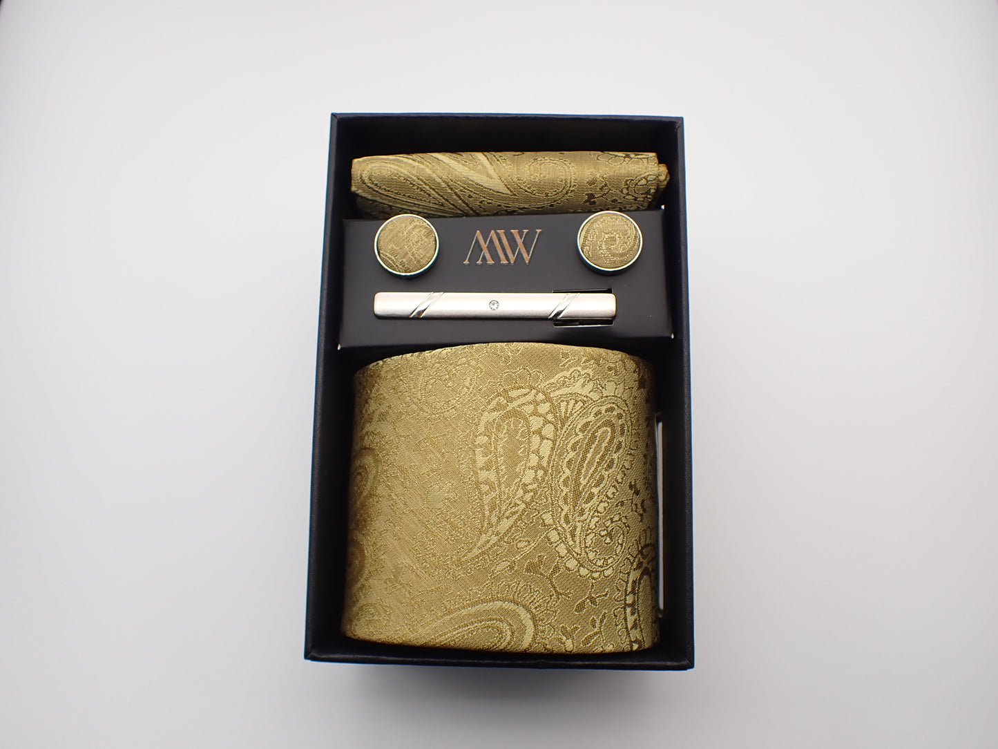 A premium black gift box containing a champagne gold paisley floral jacquard patterned men's necktie, matching pocket square, cufflinks, and a silver tie clip.