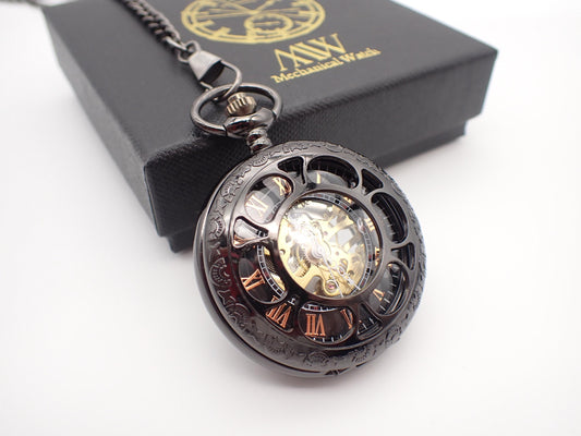 Gunmetal black skeleton pocket watch with a cut-out front cover, revealing rose gold Roman numerals and a golden hand-wind mechanical movement. Resting next to a black MW premium gift box.