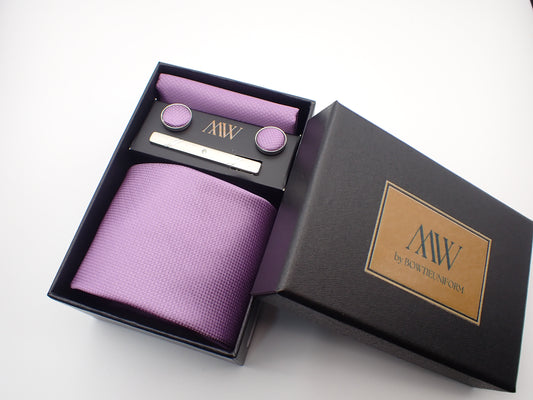 A black gift box displaying a light lavender purple textured men's necktie, matching pocket square, round cufflinks, and a silver tie clip.