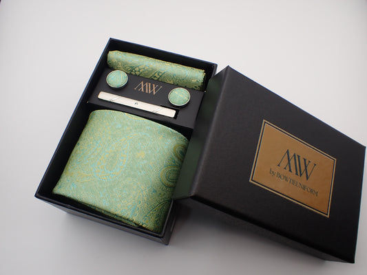 A black gift box presenting a light green and gold paisley floral jacquard patterned men's necktie, matching pocket square, cufflinks, and a tie clip.