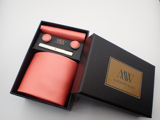 A black gift box containing a coral pink micro-woven textured men's necktie, matching pocket square, round cufflinks, and a silver tie clip.