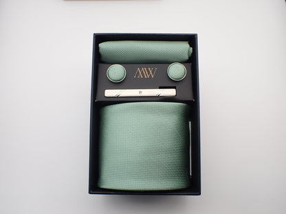 A luxury black gift box containing a pastel mint green micro-woven men's necktie, matching pocket square, cufflinks, and a silver tie clip.