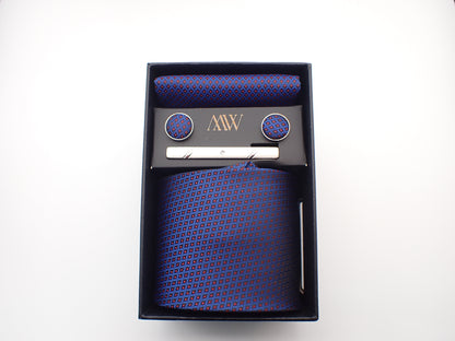 A black gift box containing a navy blue tie with small red grid checkered patterns, matching pocket square, cufflinks, and a silver tie clip.