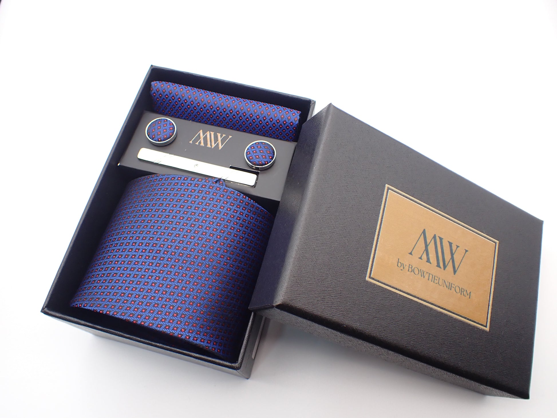 A black gift box containing a navy blue tie with small red grid checkered patterns, matching pocket square, cufflinks, and a silver tie clip.