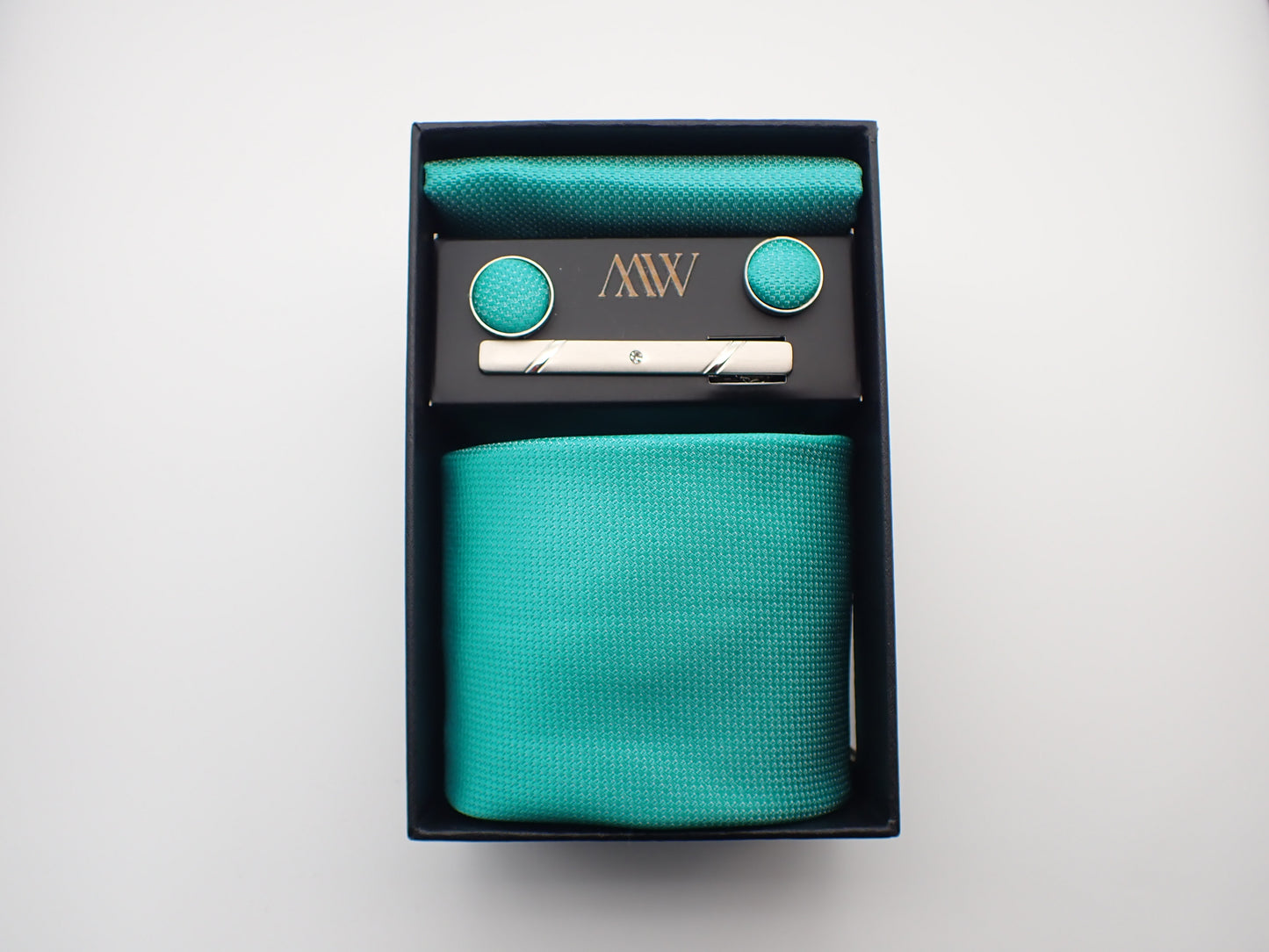 A black gift box containing a bright turquoise blue textured men's necktie, matching pocket square, round cufflinks, and a silver tie clip.
